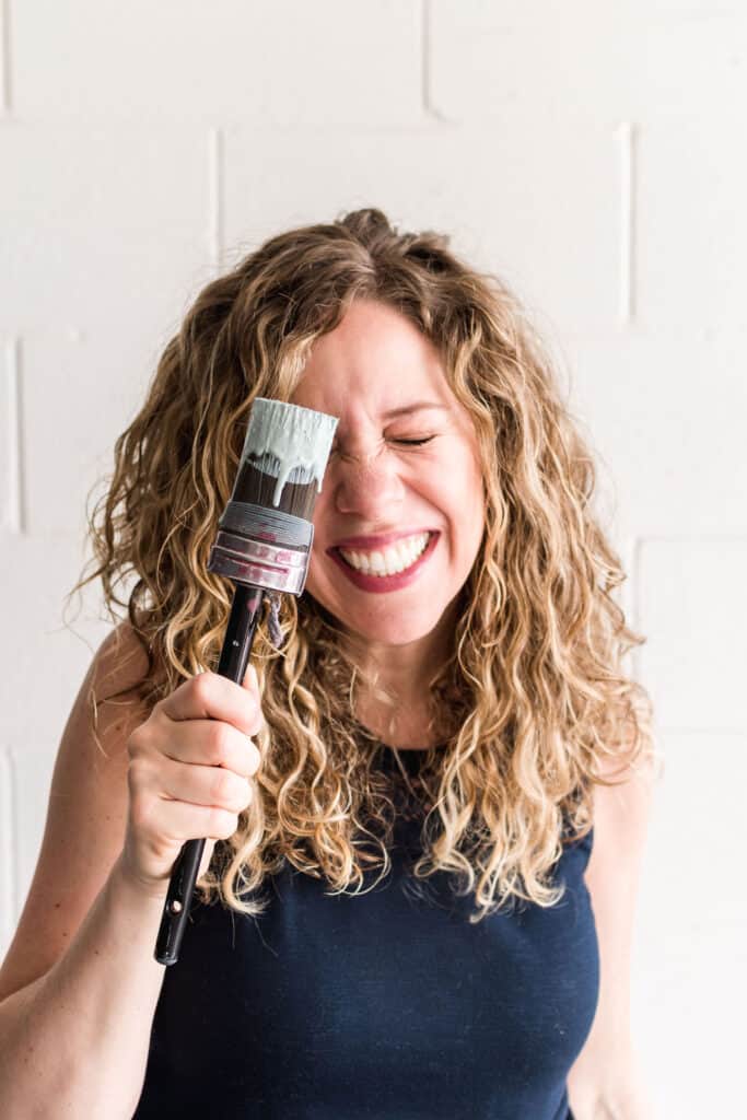Melanie Curley CEO of Mango Paint holding a paint covered brush in front of her smiling face